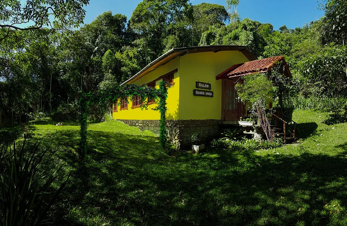 O Salão Radha Yoga por fora, amarelo entre o gramado e a mata
